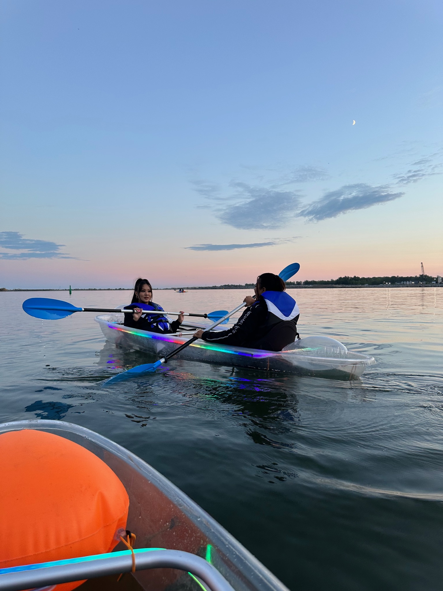 Two women paddling a rainbow LED illuminated clear kayak at sunset on Lake Ontario in Toronto - Glow-In-The-Dark Kayaking is a perfect date night idea and must-do summer activity with Illuminated Escapes