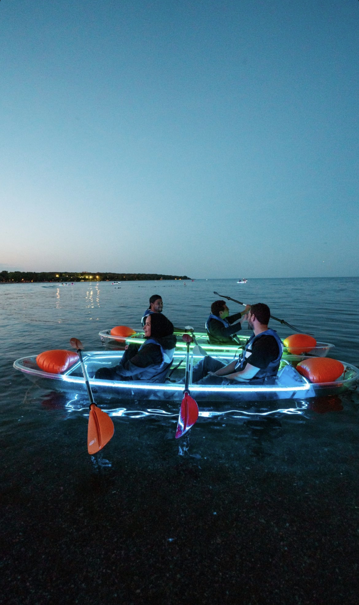 Group of four people glow in the dark kayaking at sunset in illuminated clear kayaks on calm water with Illuminated Escapes