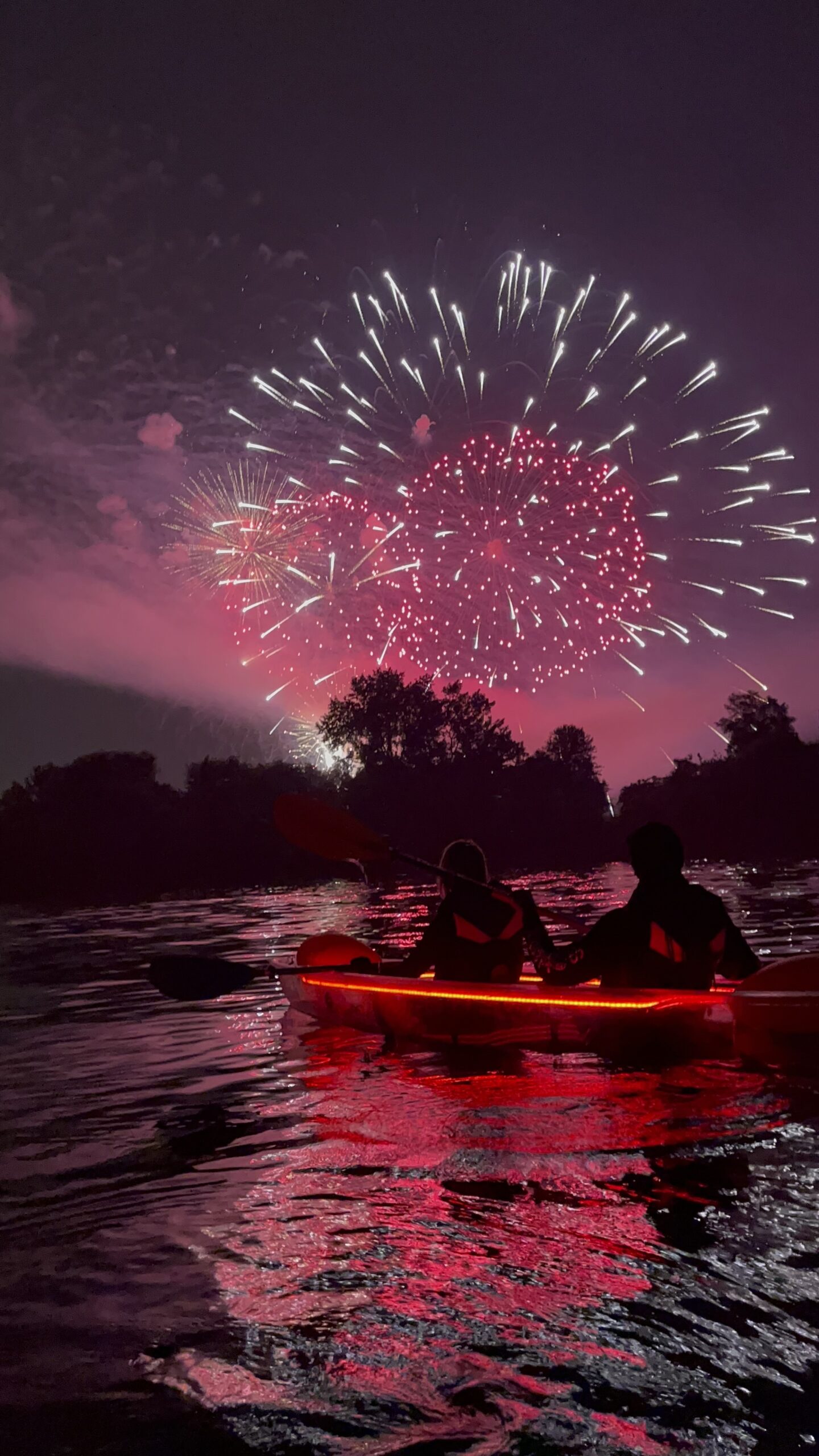 Two people watching Canada Day fireworks from a glowing red illuminated kayak on Lake Ontario in Toronto - a unique Canada Day activity with Illuminated Escapes